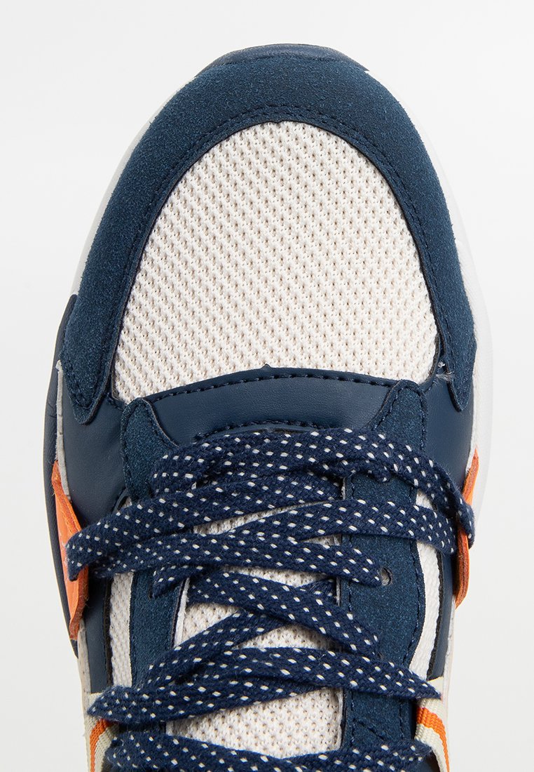 Sneaker mit einem Obermaterial aus marineblauem Wildleder und beigefarbenem Netz, ausgestattet mit marineblauen gepunkteten Schnürsenkeln, orangefarbigen Akzenten und strukturierten Seitenpaneelen.