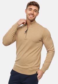 Pull en knit beige avec un col zippé mi-hauteur, des poignets et un ourlet côtelés, une coupe ajustée, une texture douce et des détails de couture subtils.