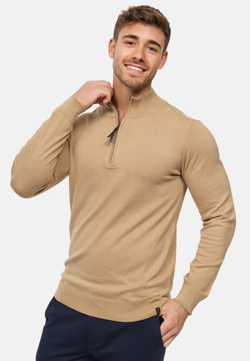 Pull en knit beige avec un col zippé mi-hauteur, des poignets et un ourlet côtelés, une coupe ajustée, une texture douce et des détails de couture subtils.