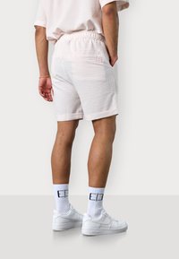 Helle rosa Shorts mit einem strukturierten Karomuster, elastischem Taillenbund und Seitentaschen, kombiniert mit weißen Turnschuhen und passenden Socken.