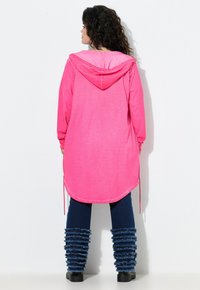 Hoodie lungo rosa con cappuccio regolabile e polsini a coste, abbinato a leggings blu navy strappati e stivali in denim con volant.
