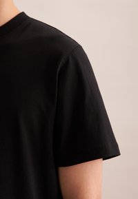 T-shirt nera a maniche corte, collo rotondo, realizzata in cotone. Presenta una superficie liscia e cuciture pulite lungo le maniche e l'orlo.