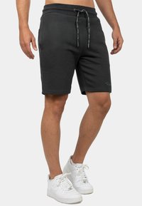 Zwarte sportieve shorts met een elastische tailleband, een trekkoord, zijzakken en een gladde textuur, gecombineerd met witte sneakers.