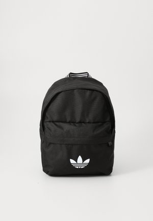 Must must seljakott, mis on valmistatud vastupidavast kangast, ees on lukuga tasku, peal on triibulised detailid ja valge kolm lehelogoga.