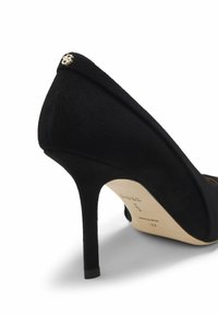 Scarpa con tacco alto in camoscio nero con punta appuntita, design curvo e dettaglio dorato sul tallone. Texture liscia e stile minimalista.