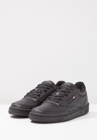 Baskets en cuir noir à surface texturée, bout rond et design à lacets. Dotées d'un col rembourré et du logo Reebok sur le côté.