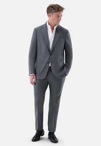 Grau maßgeschneiderter Anzug mit Revers, zwei Knöpfen und Fronttaschen; kombiniert mit einem weißen Hemd und schwarzen Lederschuhen. Glatte Textur.