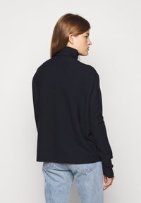 Mørkeblåpolo genser laget av strikket stoff, med avslappet passform og lange ermer, kombinert med lyseblå denimbukser.