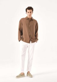 Rjava srajca s gumbi in ovratnikom, bele ozke hlače ter svetlo rjavi natikači. Gladek material z ohlapnim krojem.