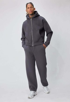 Sweat à capuche gris en polaire avec fermeture éclair et poches kangourou, associé à un pantalon ample assorti. Le matériau semble doux avec une texture lisse.