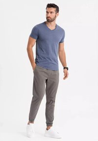 Šedé joggers kalhoty s elastickými manžetami, spárované s modrým tričkem s výstřihem do V vyrobeným z měkkého materiálu. Bílé tenisky doplňují celý outfit.