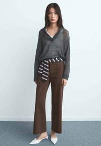 Pull en maille gris avec un col en V, associé à un pantalon ample marron taille haute et une ceinture à rayures. Des ballerines blanches à bout pointu complètent la tenue.