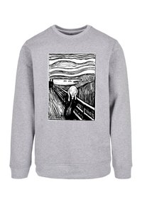 Szürke kapucnis pulóver, amelyen fekete nyomat látható Edvard Munch "A sikoly" című művéről, amely egy alakot ábrázol, amint kezét az arcára tapasztja, egy örvénylő háttér és víz előtt.