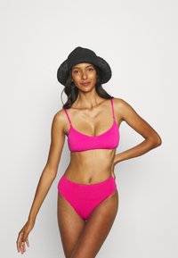 Biquíni rosa texturizado com alças finas e parte de baixo de cintura alta, combinado com um chapéu de balde preto trançado.