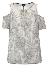 Valkoinen paita, jossa on kylmät olkapäät ja monimutkaiset mustat kukkakuviot. Valmistettu kevyestä materiaalista, jossa on pyöreä kaula-aukko ja aaltoileva helma.