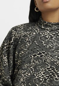 Haut imprimé noir et beige avec un col haut, présentant un design à motif animal textur�é. Accentué par de grandes boucles d'oreilles créoles.