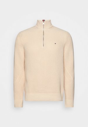 Beżowy sweter dzianinowy z kołnierzem na zamek błyskawiczny do połowy, z prążkowanymi mankietami i dołem, z małym logo flagi po lewej stronie klatki piersiowej.