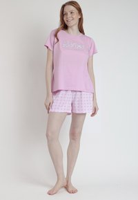 Conjunto de pijama de algodón rosa que incluye una camiseta de manga corta con el texto "Barbie" y pantalones cortos de patrón a cuadros en tonos rosa claros.