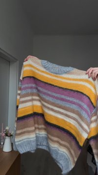 Sweter z dzianiny w różnych kolorach, z szerokimi poziomymi paskami w kolorach żółtym, fioletowym, szarym i brązowym. Luźny krój i ściągacze na mankietach.