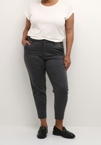 Grå skräddarsydda byxor med en avsmalnande design, sidofickor och en slät yta, kombinerat med en vit t-shirt och svarta loafers.