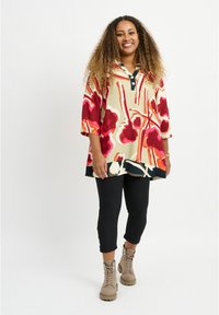 Tunic floreale in tonalità crema, rosso e rosa con collo a camicia, maniche tre quarti e dettagli neri, abbinata a leggings neri e stivali.