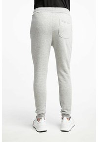 Pantalons de survêtement gris avec une coupe ajustée, une taille élastique et une poche arrière unique. Le matériau semble doux et texturé, associé à des baskets blanches.