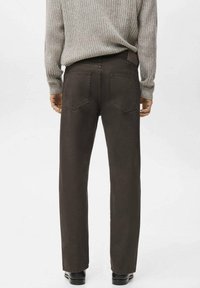 Pantalones marrones de corte recto con dos bolsillos traseros y detalles sutiles de costura, combinados con un suéter gris texturizado.