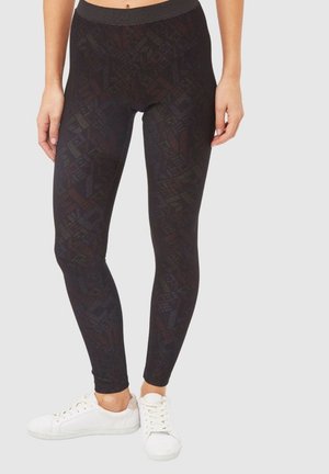 Mallas negras con un patrón geométrico, hechas de material elástico con una cintura alta, combinadas con zapatillas blancas.