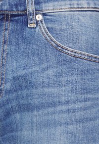 Ljust blå denimjeans har en klassisk femficksdesign, med synlig sömnad och en metallknapp i midjan.