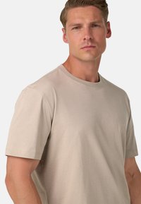 Krátky rukáv, kruhový výstrih, tričko v béžovej farbe z bavlny s hladkou textúrou a voľným strihom. Minimalistický dizajn bez viditeľných vzorov alebo log.