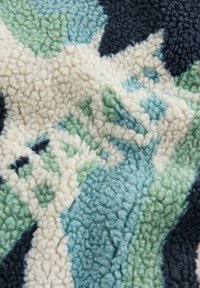 Pūkaina, mīksta auduma materiāls ar daudzkrāsainu abstraktu rakstu tumši zilā, gaiši zaļā un krēmkrāsas toņos. Mīksta, teksturēta virsma.