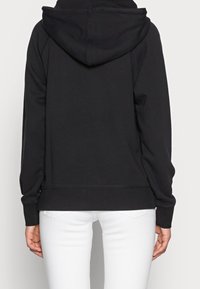 Sudadera negra con capucha y corte relajado, que cuenta con un bolsillo canguro y puños acanalados. Textura suave y detalles de costura mínimos.