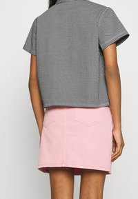 Camicia corta a maniche corte a motivo pied de poule bianco e nero, abbinata a una gonna di denim rosa chiaro con tasche posteriori e taglio dritto.