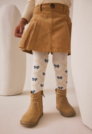 Tan corduroy plisseret nederdel, hvide sokker med marineblå sløjfer og brune ankelsko med dekorativ syning og lynlåsdetalje.