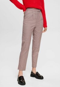 Rutiga bruna och gräddfärgade byxor med framfickor och smal benställning, tillsammans med en röd stickad tröja och svarta loafers.