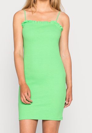 Robe sans manches vert clair ajustée avec bretelles fines et col à volants portée par une femme sur un fond uni.