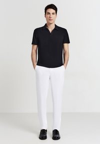 Polo shirt nera a maniche corte con colletto, abbinata a pantaloni bianchi su misura e mocassini neri. Texture semplice e liscia con linee pulite.