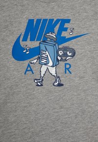 Szürke póló, amelyen egy cipős doboz és egy boombox stílusú mesehős látható, kék Nike logóval és vastag betűkkel írt "AIR" felirattal.