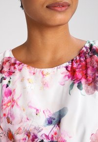 Floral blouse featuring a white base with pink and purple watercolor flower patterns, soft fabric, and a round neckline.