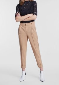 Beige skræddersyede bukser med opsmøg, parret med en navy blonde top. Modellen bærer hvide ankelstøvler med en sort detalje.