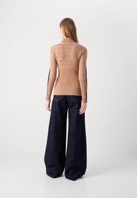 Langsleeve, geribbelde top in lichtbruin, met horizontale strepen. Gecombineerd met wijde, donkere denim jeans, die een casual pasvorm laten zien.