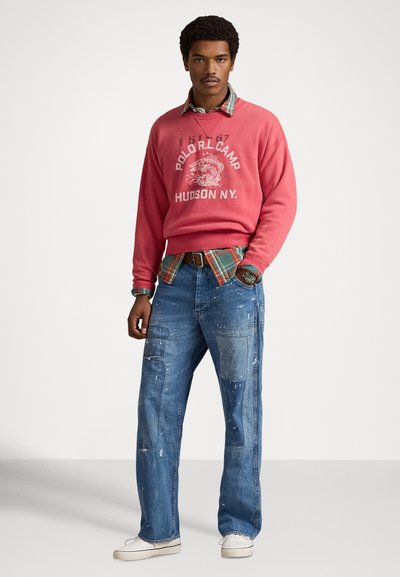 Rosa genser med hvitt trykk, lagvis over en rutete skjorte. Blå jeans med slitte detaljer og lapper. Casual hvite sko.