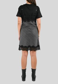 Maglietta nera sovrapposta a un vestito grigio a fantasia. Il vestito presenta un bordo in pizzo nero all'orlo. Stivali neri alla caviglia completano l'outfit.
