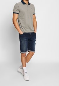 Szara koszulka polo z krótkim rękawem i granatowym kołnierzykiem oraz mankietami, zestawiona z ciemnymi szortami dżinsowymi, zakończonymi na wysokości kolan, oraz białymi tenisówkami.