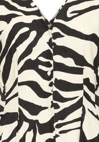 Tissu imprimé zèbre noir et blanc avec un col en V et trois petits boutons blancs au centre.