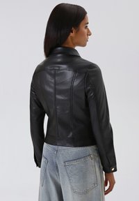Giacca di pelle nera con un design aderente, colletto appuntito e dettagli di cucitura ben visibili. Abbinata a jeans a vita alta di colore azzurro chiaro.