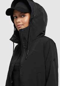 Svart zip-up jacka med huva, med hög krage, dragsko och logodetaljer. Slät textur och figurnära design.
