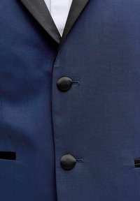 Tuva zilas krāsas smokinga žakete ar melni satīna apdari pie atloka un melniem satīna pārklātiem pogām.