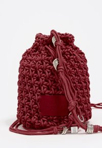Bolsa de cordón en color marrón con un patrón tejido, hecha de tela y cordón. Presenta herrajes en tono plateado y una etiqueta de acento de cuero.