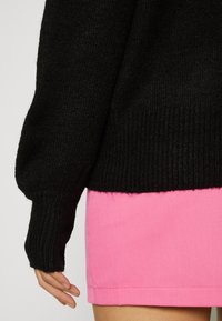 Schwarzer Strickpullover mit Rippbündchen, kombiniert mit einem leuchtend pinken Rock. Der Pullover hat eine lockere Passform und strukturierte Stoffdetails.